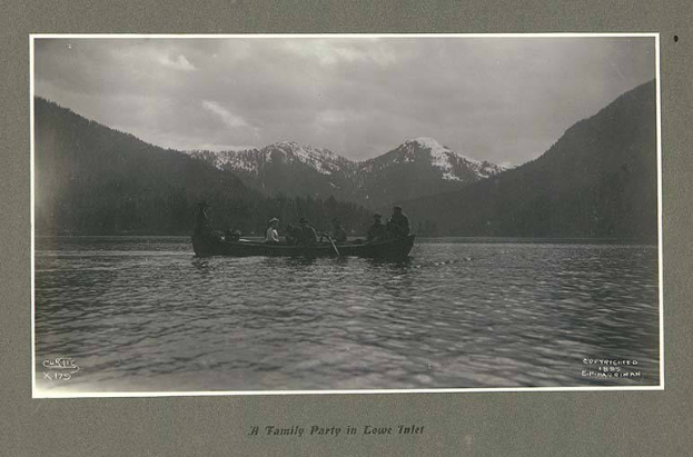 Schwarzes und weißes Foto einer Familie in einem Kanu auf einem See mit Bergen und Bäumen im Hintergrund, Himmel oben sichtbar und Text unten.