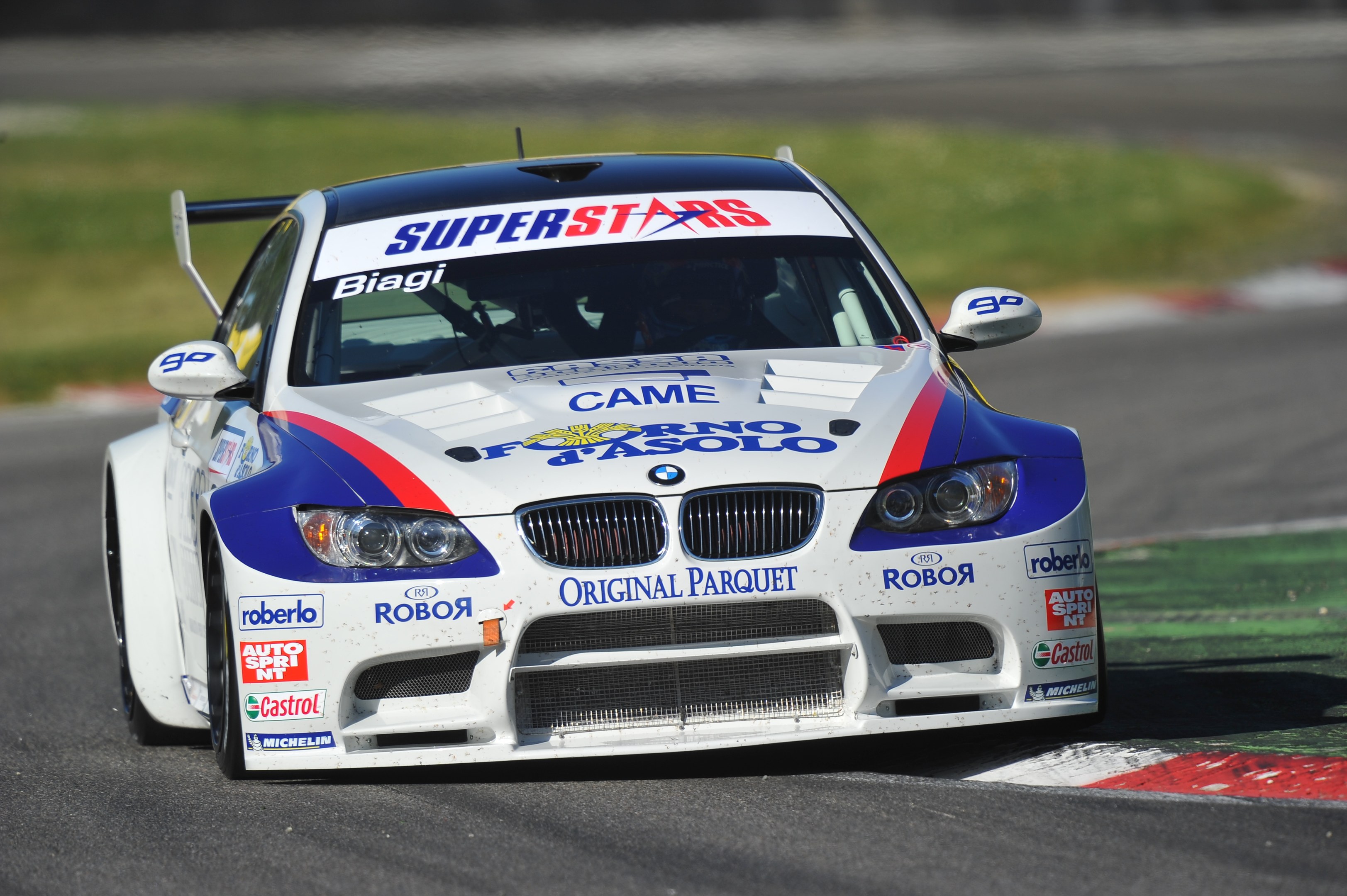 Ein BMW M3 GT3 Rennauto in Bewegung auf einer unscharfen Rennstrecke mit grasigem Umfeld.