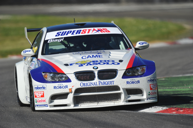 Ein BMW M3 GT3 Rennauto in Bewegung auf einer unscharfen Rennstrecke mit grasigem Umfeld.