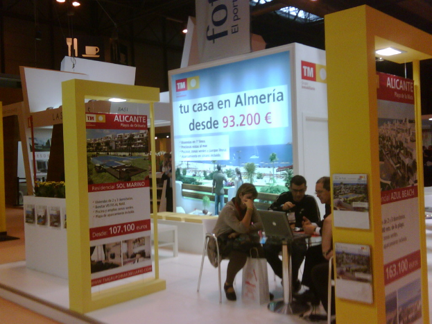 Ein Raum mit Menschen an einem Tisch, die auf Laptops arbeiten, umgeben von Flyern mit verschiedenen Anzeigen.