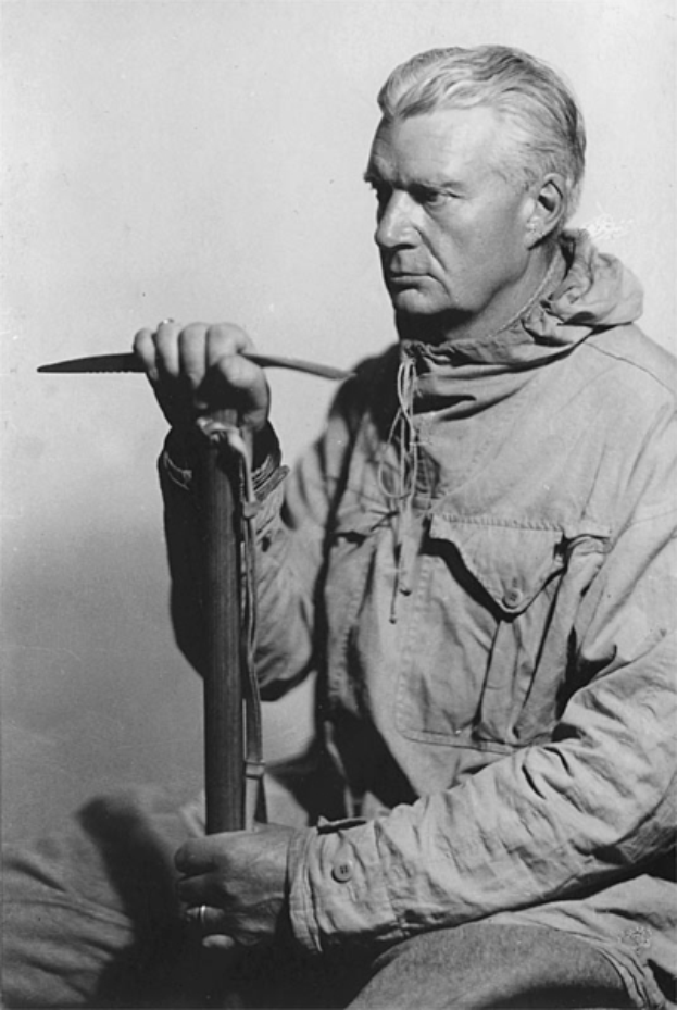 Ein altes Schwarz-Weiß-Foto eines Mannes in einem langärmligen Hemd und Hose, mit zurückgekämmtem Haar, der ein Messer hält und konzentriert auf die Klinge schaut.