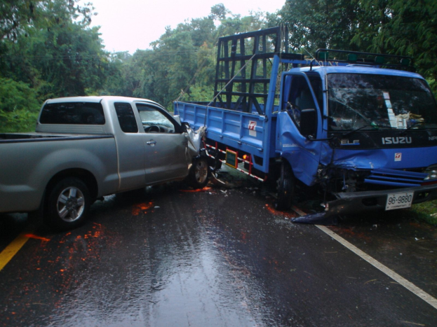Ein schwerbeschädigter Lkw mit eingedellter Front und verbeulter Karosserie liegt am Straßenrand, umgeben von Bäumen unter einem klaren blauen Himmel.