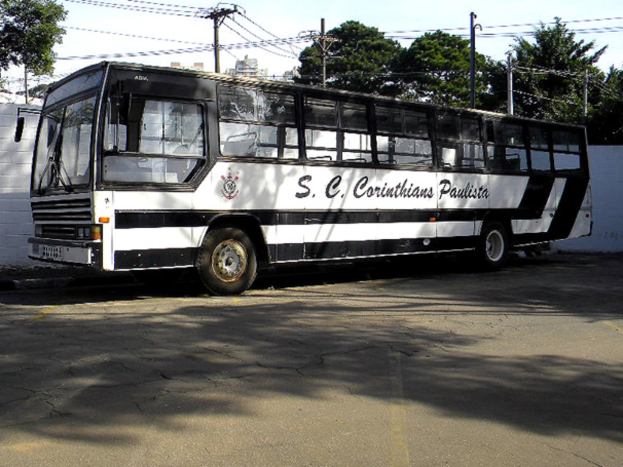 Ein Bus steht auf einer Straße mit einer Wand, Strommästen mit Kabeln, Bäumen, Gebäuden und dem Himmel im Hintergrund.