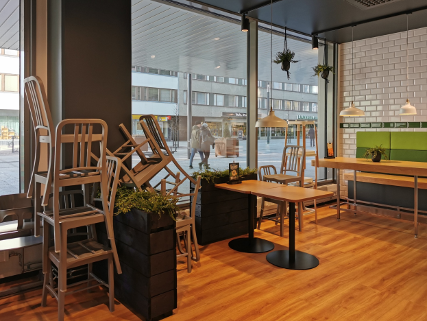 Ein Berliner Restaurant mit hölzernen Tischen und Stühlen vor einem großen Fenster, das auf eine Straße mit Fußgängern, Gebäuden und städtischen Elementen blickt.