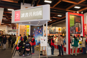 Eine große Gruppe von Menschen an einem Messestand mit Stühlen, Texttafeln, Bannern und Deckenleuchten, die "Book Republic Hong Kong Book Fair" lesen.