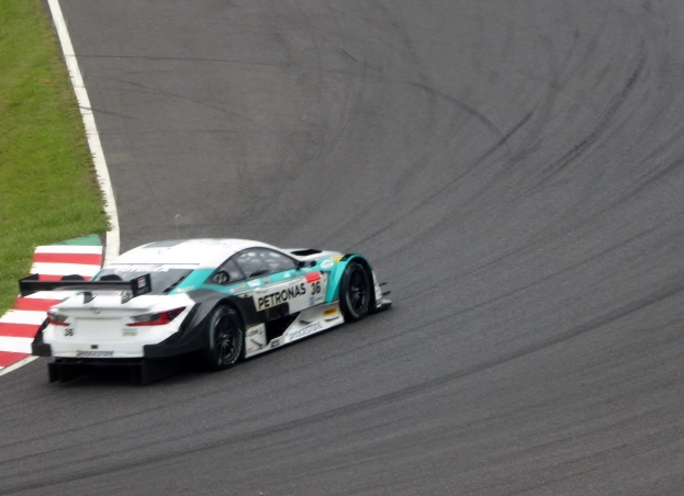 Ein silberner Mercedes-AMG GT3-Rennwagen mit Sponsorentext auf der Karosserie, der auf einer Rennstrecke fährt, mit Gras links sichtbar.