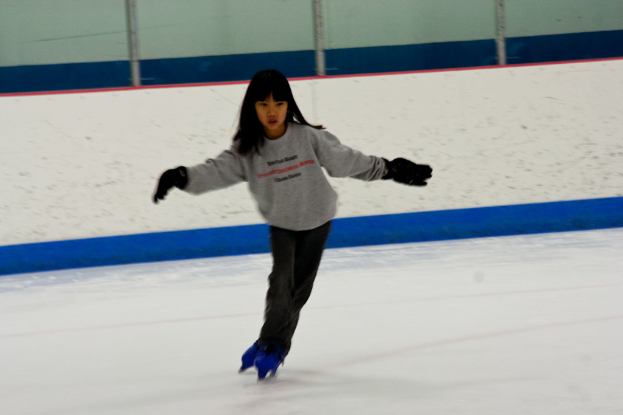 Eine Person in Kleidung fährt auf Eis mit Stöcken, die oben im Bild zu sehen sind.