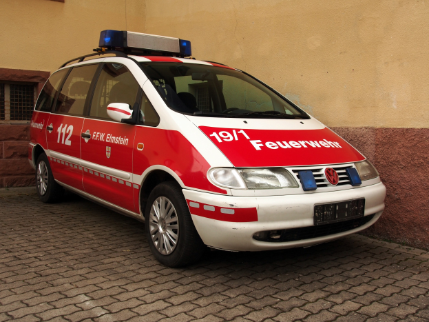 Ein roter und weißer Minivan, der als Krankenwagen markiert ist, steht vor einem Fenster mit Fenstern.