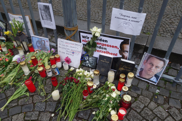 Gedenken in Berlin mit Blumen, Kerzen, Fotos und Plakaten vor einem Zaun.