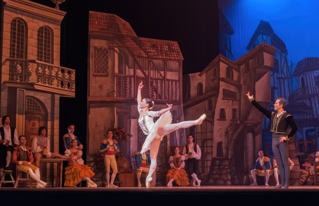 Zwei Tänzer performen auf einer Bühne im Royal Opera House in London, mit einem sitzenden und stehenden Publikum im Vordergrund.