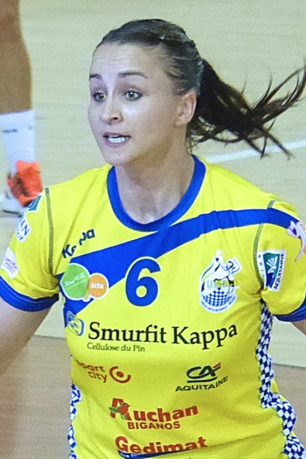 Eine Frau in einer gelben und blauen Uniform spielt Volleyball, wobei ein menschlicher Unterschenkel im Hintergrund zu sehen ist.