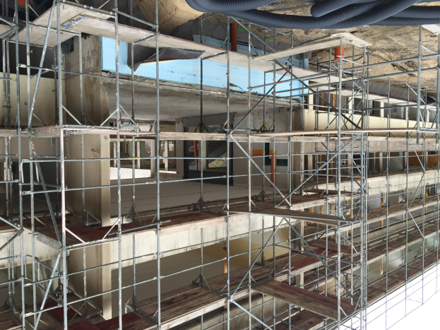 Ein unter Baugerütestügen aus Metallstäben und Holzplanken sowie an der Decke verlaufenden Rohren gebautes Gebäude.