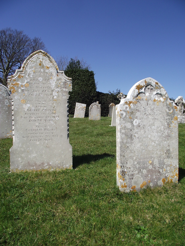 Ein Friedhof mit zahlreichen Gräbern, Gras auf dem Boden und Bäumen mit Himmel im Hintergrund.