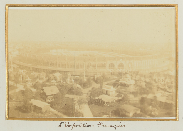 Altes Foto eines Stadions in städtischer Umgebung mit umliegenden Gebäuden, Bäumen und Pfählen, mit Text unten.