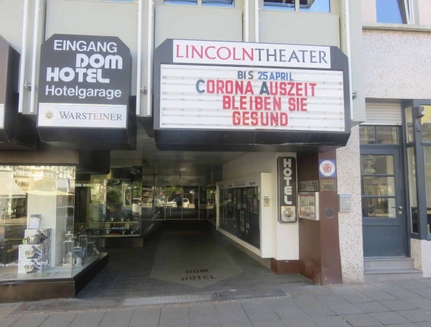 Das Lincoln Theater in Berlin, Deutschland, ein Gebäude mit Glasfenstern und -türen und einer Tafel mit Text darauf, das verschiedene Objekte im Inneren zeigt und so einen Eindruck von einer pulsierenden Stadtlandschaft vermittelt.