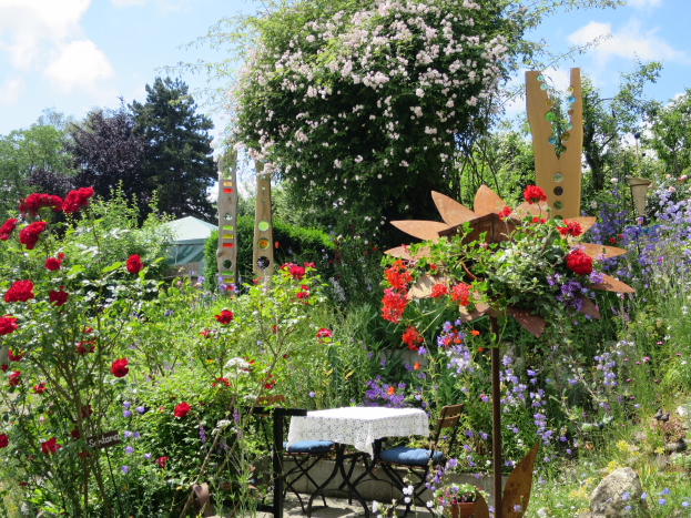 Ein Garten mit bunten Blumen und Pflanzen, der einen Tisch und Stühle mit einer Decke zeigt, umgeben von Bäumen unter einem bewölkten Himmel auf der Chelsea Flower Show.