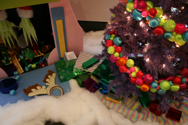 Eine Indoor-Szene mit einem dekorierten Weihnachtsbaum auf der rechten Seite, Geschenkboxen und Deko in der Mitte und einer H├╝tte mit Deko in der oberen linken Ecke, mit W├Âlldecke und Schafwolle unten.