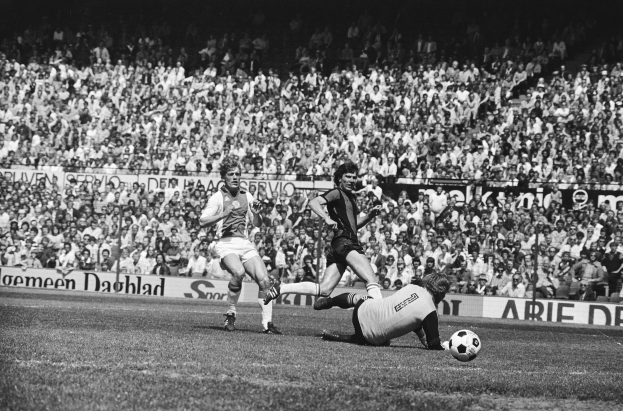 Schwarzes und weißes Foto von Männern, die auf einem Feld Füßball spielen, mit Zuschauern im Hintergrund und einer 'Bundesliga 1978-79 Ajax 1-1 Hannover 96' -Fahne.