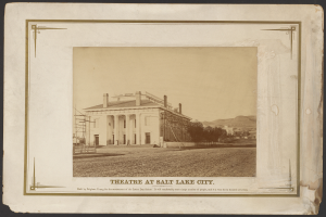 Ein Schwarz-Weiß-Foto des Theaters in Salt Lake City, mit einem Gebäude in der Mitte umgeben von Bäumen und Hügeln im Hintergrund und Text unten.