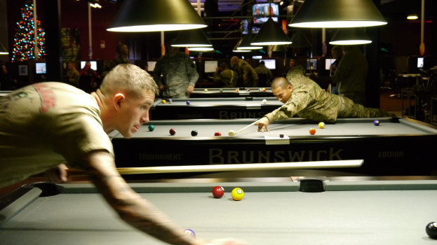 Ein Raum mit Snookertischen, Spielern auf beiden Seiten, hängenden Lampen, einem Weihnachtsbaum in einer Ecke und Bildschirmen mit Anzeigen.