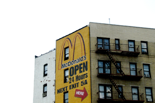 Ein Gebäude mit Text und einem Gemälde an der Wand, das Treppen, Geländer und Klimaanlagen an den Fenstern zeigt, unter einem Himmel mit sichtbarem Rohr.