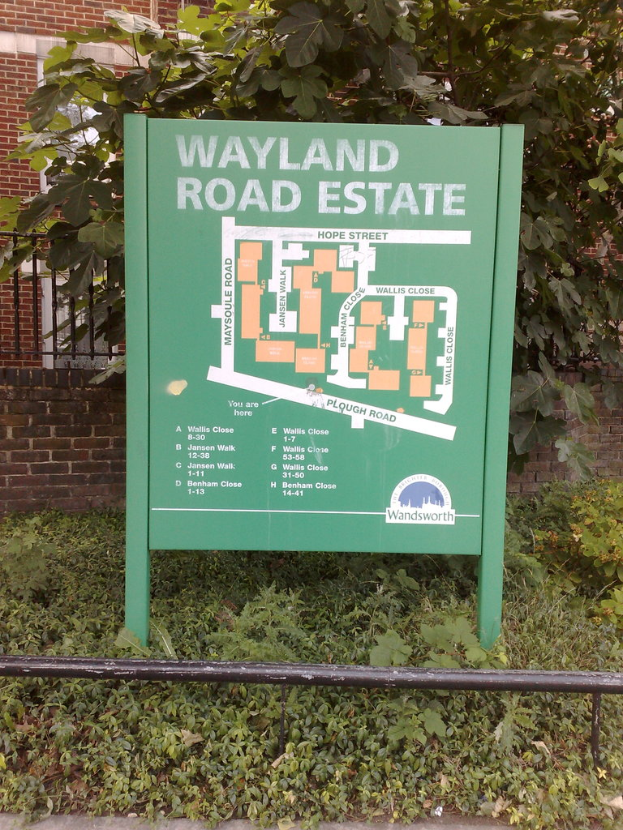 Eine grüne Straßenzustandsplanungstafel, die eine Karte zeigt, mit Gras, einem Baum, einem Gebäude und einem Grill im Hintergrund.