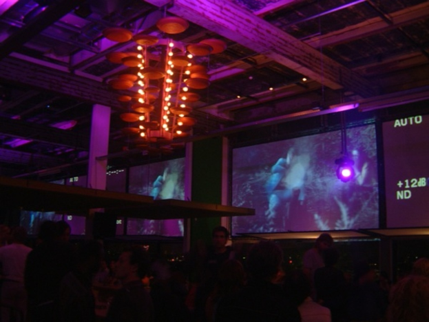 Eine Gruppe von Menschen in einem Raum mit Bildschirmen, Lampen, Stangen und einer Decke hängenden Kronleuchter.