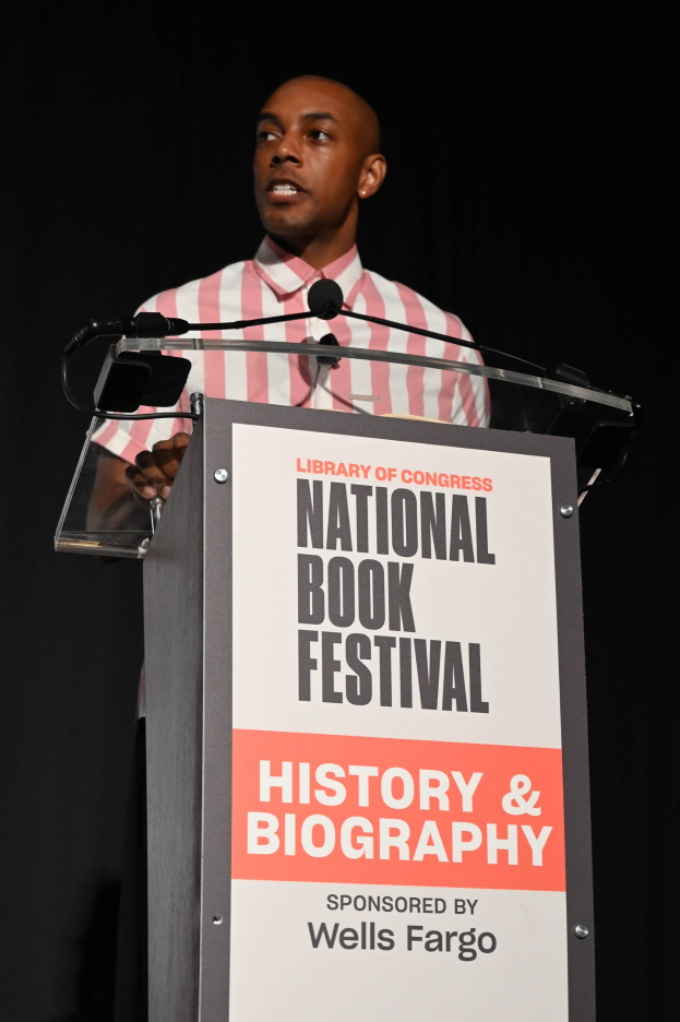 Ein Mann steht an einem Rednerpult mit einem Mikrofon und spricht bei einer Abendveranstaltung mit dem Titel "National Book Festival Geschichte & Biografie".