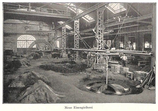 Altes Schwarz-Weiß-Foto einer Fabrik mit Arbeitern, die an einer Maschine arbeiten, umgeben von Metallstangen und -pfählen, mit der Beschriftung 'Neue Eisenglebeerei, die erste Fabrik in Deutschland' unten.