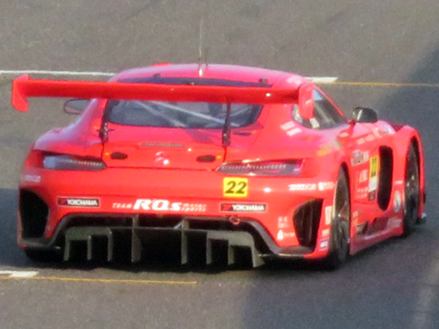 Roter Porsche 911 GTS Rennwagen auf einer Rennstrecke mit aerodynamischem Design, großem Heckflügel und schwarzen Rädern.