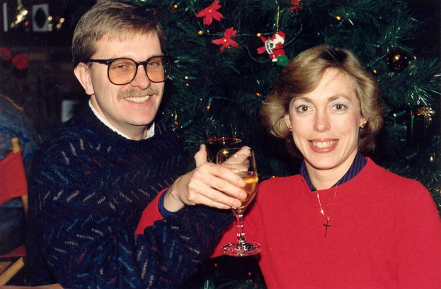 Ein Paar lächelt, waßrende es Gläser Wein hält, mit einem Weihnachtsbaum im Hintergrund.