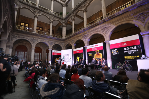 Eine Gruppe von Menschen, die an einem Tisch mit einem Podium und einem Mikrofon vor einer Menge, Kameras und Bannern sitzen, was eine Pressekonferenz für das CDMX 2017-Ereignis suggeriert.