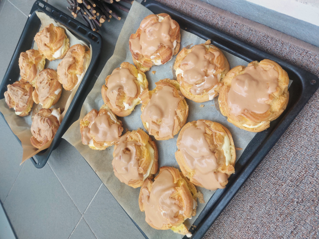 Ein Tablett voller gemischter dänischer Kekse mit hellgoldener Farbe und flaky Textur, einige mit Puderzucker bestäubt, liegt auf einer Theke neben einem offenen Fenster und wird von warmem Licht beschienen.
