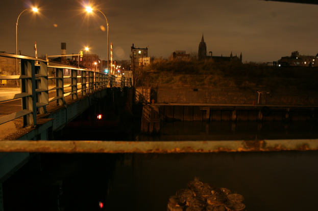 Eine Brücke überspannt einen Fluss mit zahlreichen Straßenlaternen darauf und viele Gebäude sind im Hintergrund zu sehen.