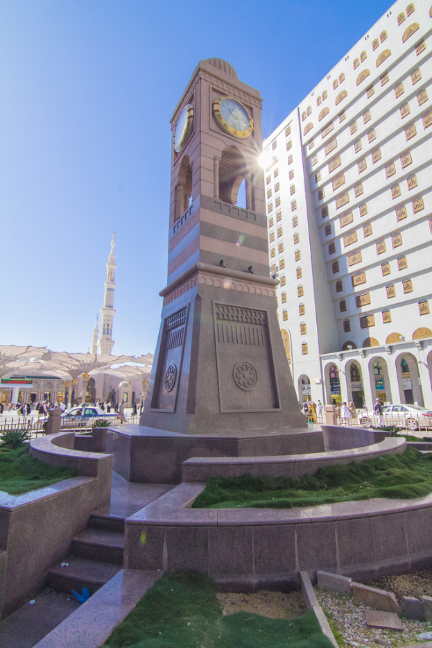 Ein Uhrturm in der Mitte mit einem großen Gebäude auf der rechten Seite.