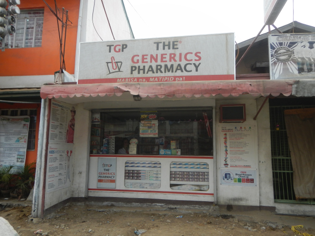 Außensicht der The Generics Pharmacy Filiale mit umliegenden stadtelementen unter einem klaren blauen Himmel.
