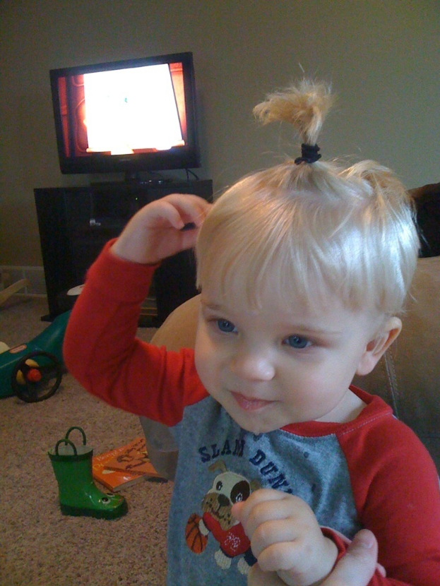 Eine Person, die ein Kind hält, mit einem Monitor auf einem Ständer, einer Couch und diversen Gegenständen im Hintergrund.