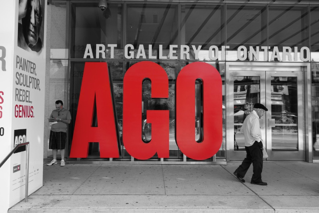 Ein Mann steht mit einem Notizbuch in der Hand und schreibt in der Nähe der gläsernen Kunstgalerie des Ontario Art Gallery of Ontario, während ein anderer Mann daneben geht.