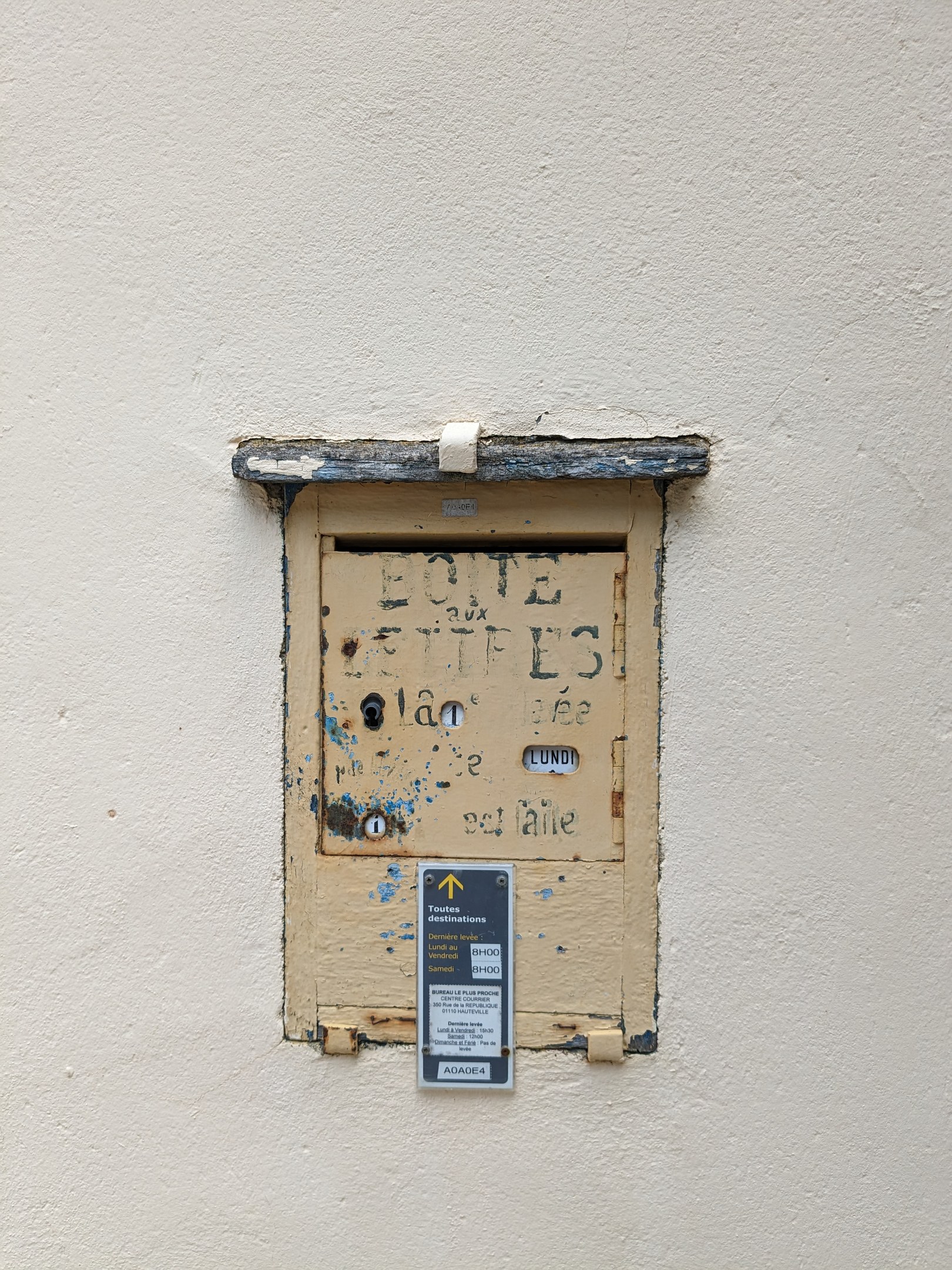 Alte rechteckige Metallklingel mit einem Schlüsselloch und einem Schild, angebracht an einer verwitterten Gebäudewand mit sichtbaren Rissen und Absplitterungen.