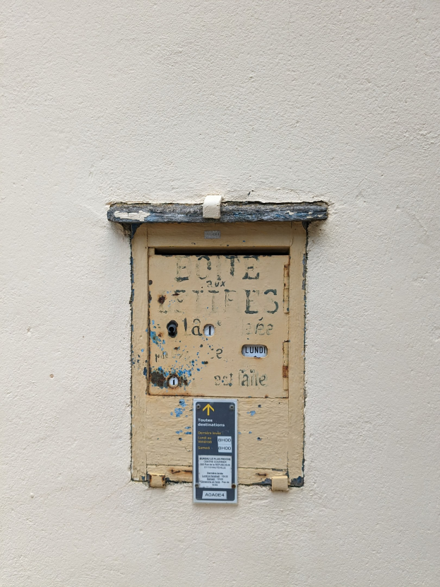 Alte rechteckige Metallklingel mit einem Schlüsselloch und einem Schild, angebracht an einer verwitterten Gebäudewand mit sichtbaren Rissen und Absplitterungen.