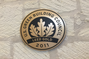 Das Logo der U.S. Green Building Council an einem Gebäude, das ein grüner Schild mit weißer Umrandung und fettem schwarzen Text zeigt, umgeben von einem Lorbeerkranz.