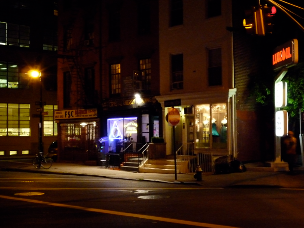 Eine Stadtstraße mit Gebäuden, Geschäften, Bäumen, einer Straße, einem Fahrrad, Treppen und einer Ampel, alles beleuchtet von Lichtern.