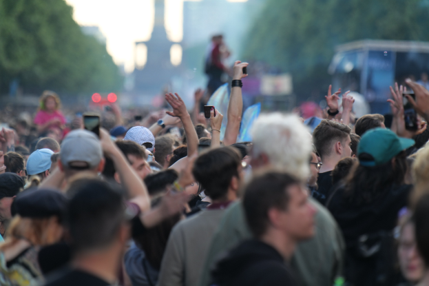 Menschenmenge auf einem Musikfestival mit erhobenen Händen, einige tragen Mützen und halten Telefone.
