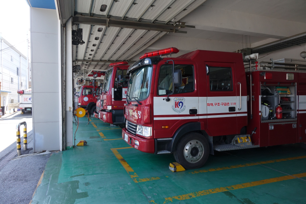 Feuerwehrfahrzeuge in einer Parkgarage geparkt mit einem Gebäude auf der linken Seite und anderen Fahrzeugen auf der Straße, vor einem Hintergrund von Gebäuden, Polen, Drähten und dem Himmel.