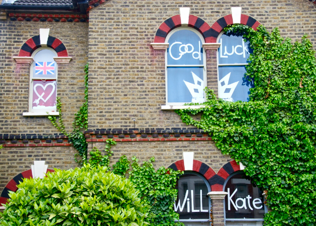 Ein Gebäude mit grünen Blättern im Vordergrund, das Fenster mit Fahnen, Plakaten und Text zeigt.