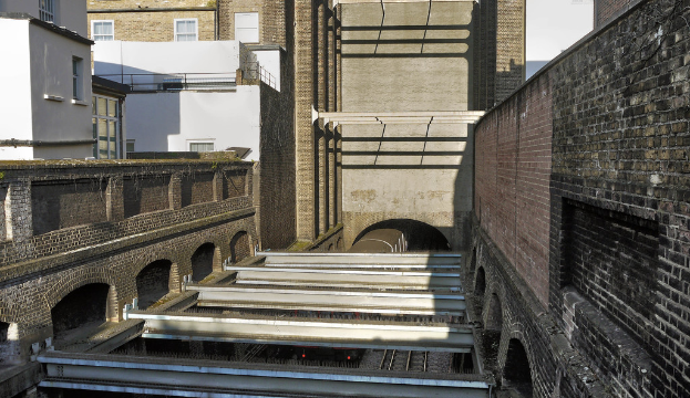 Ein Zug fährt aus einem Tunnel mit Gebäuden im Hintergrund.